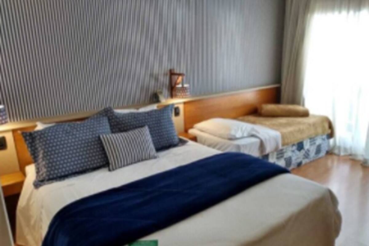 A hotel room with a large bed, a smaller bed, a nightstand, and a window with curtains.