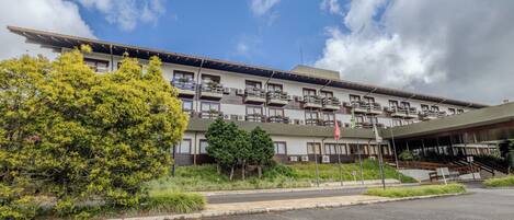 Hotel com vários andares, varandas, entrada coberta e área de estacionamento.