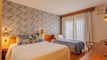 Une chambre d’hôtel avec deux lits, un bureau en bois, une table de chevet et un mur orné d’un motif floral.