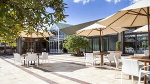 An outdoor patio area with tables and chairs, large umbrellas, and a glass building in the background. - Serra Alta Hotel (Sao Bento do Sul)