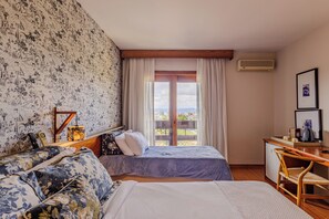 Habitación de hotel con cama, escritorio, una silla, ventana con cortinas y papel tapiz con estampado.