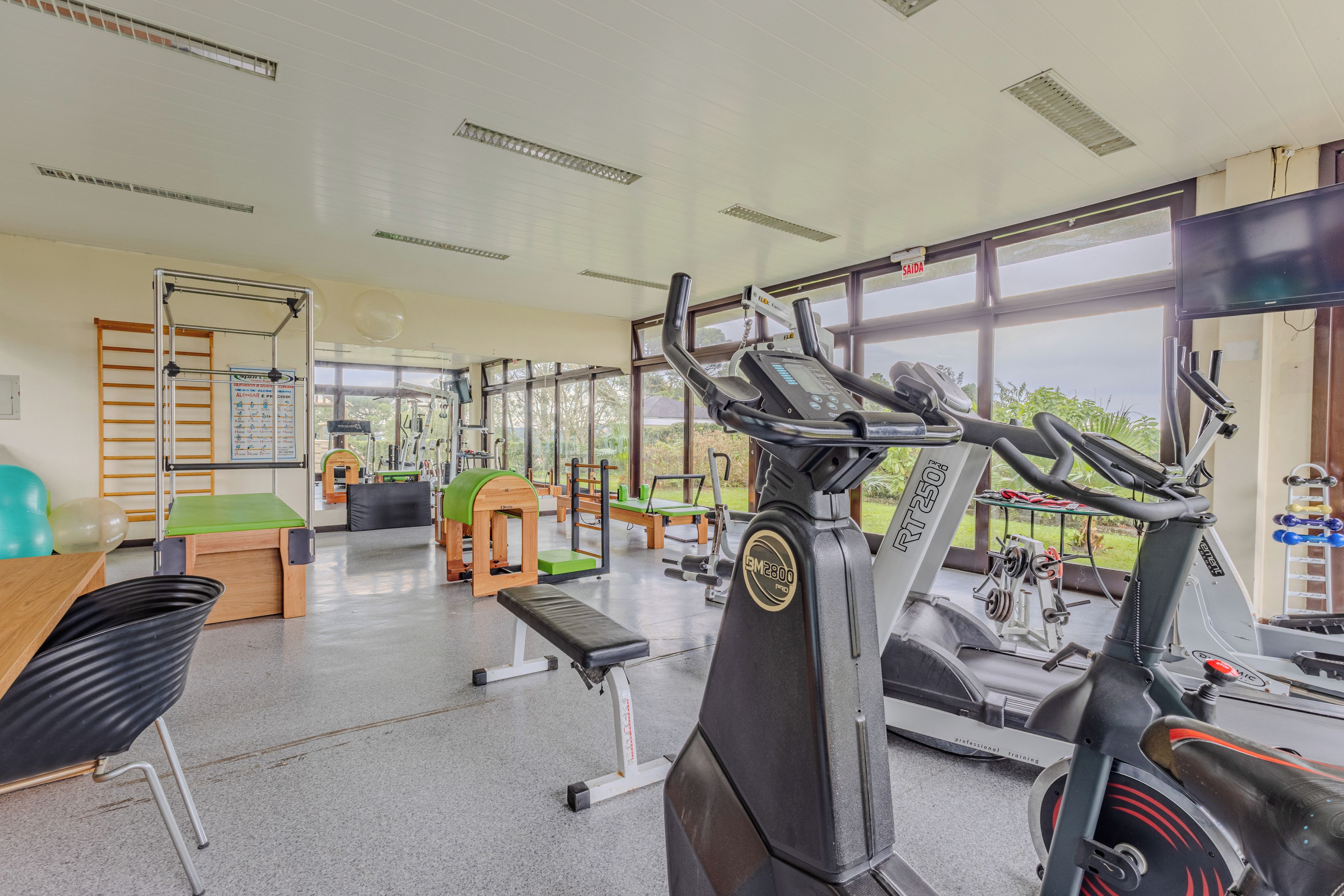 A gym with exercise equipment, a bench, and a window with a view of greenery.