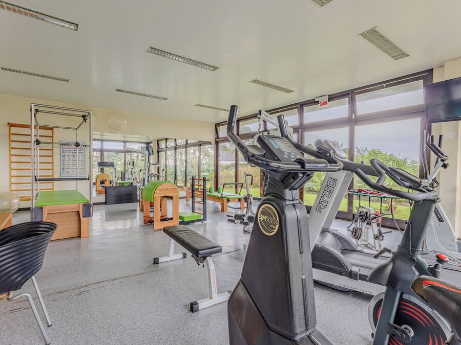 Un gimnasio con equipo de ejercicio, una banca y una ventana con vistas a la vegetación.