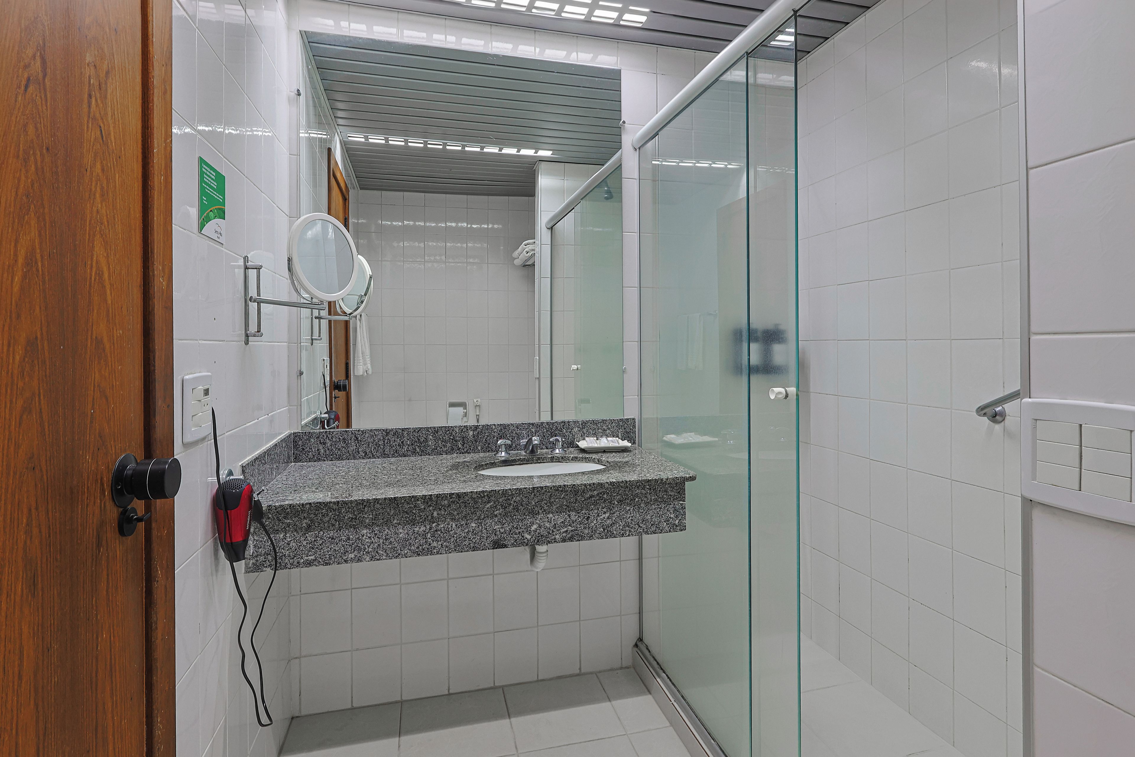 Un baño con encimera de granito, cabina de ducha con mampara de vidrio y puerta de madera.