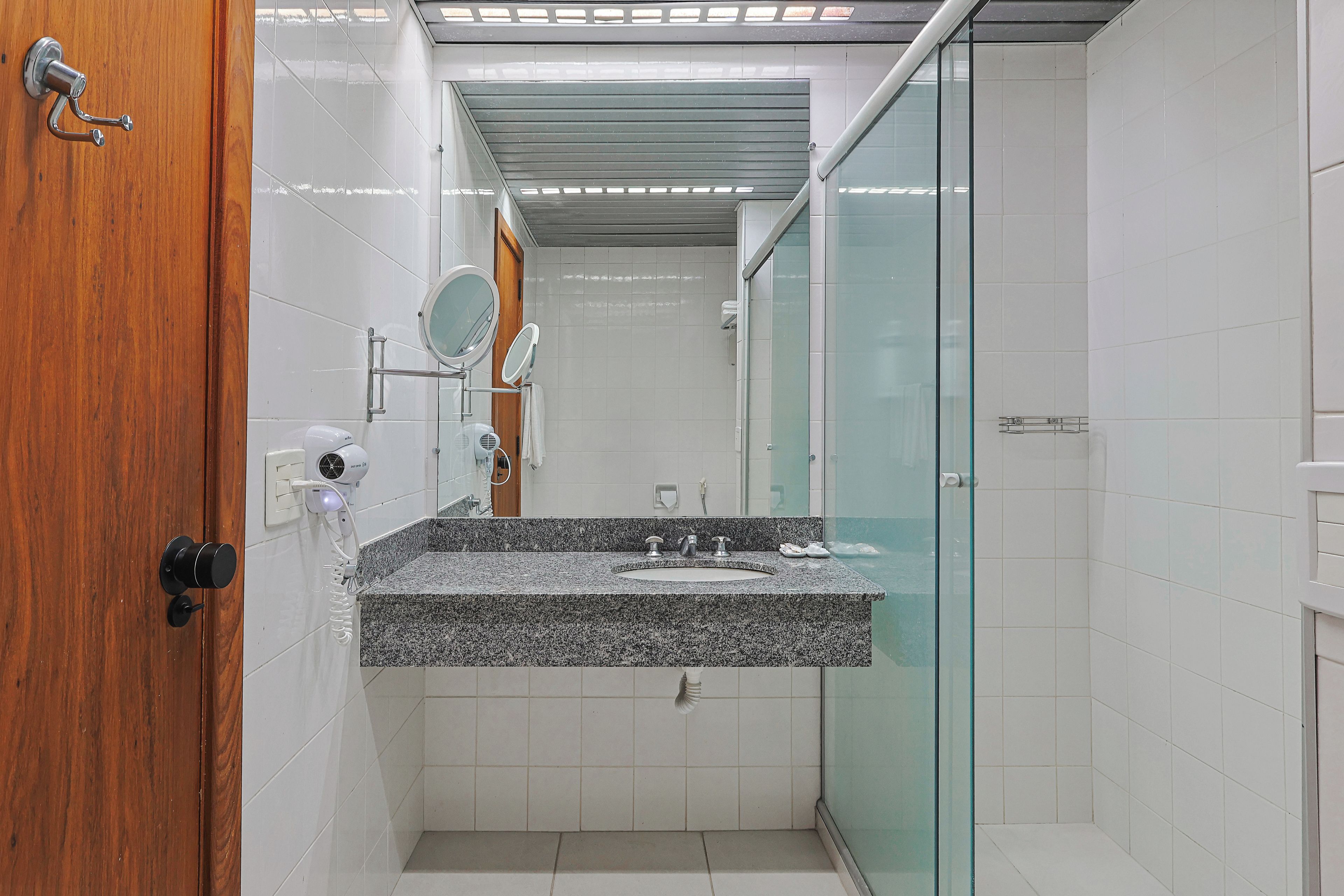 Un baño moderno con encimera de granito, cabina de ducha de vidrio y puerta de madera.