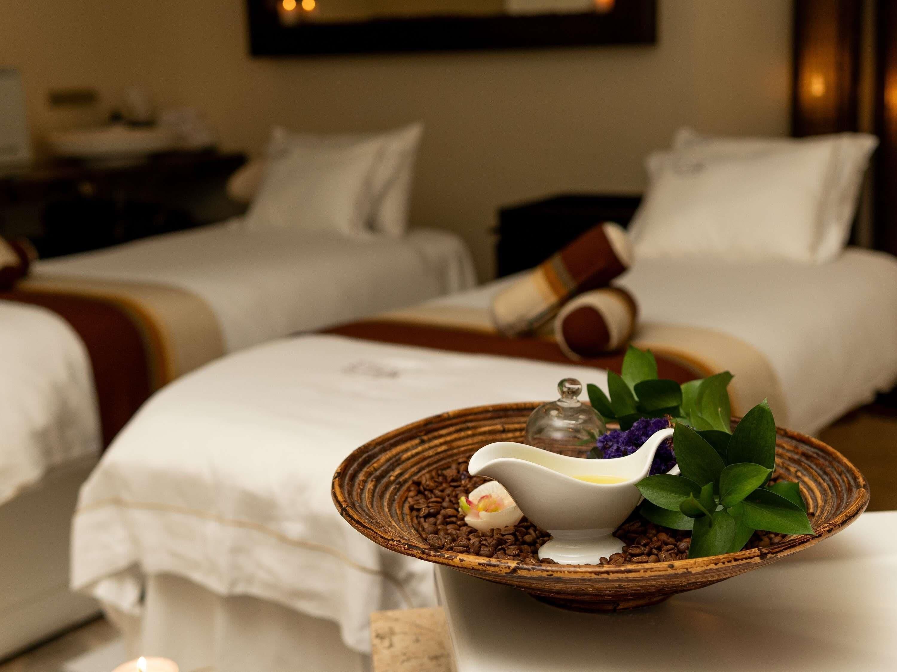 A hotel room with two beds, a small table with a bowl of coffee beans, a decorative item, and a plant.