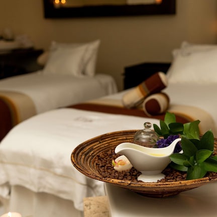 A hotel room with two beds, a small table with a bowl of coffee beans, a decorative item, and a plant.