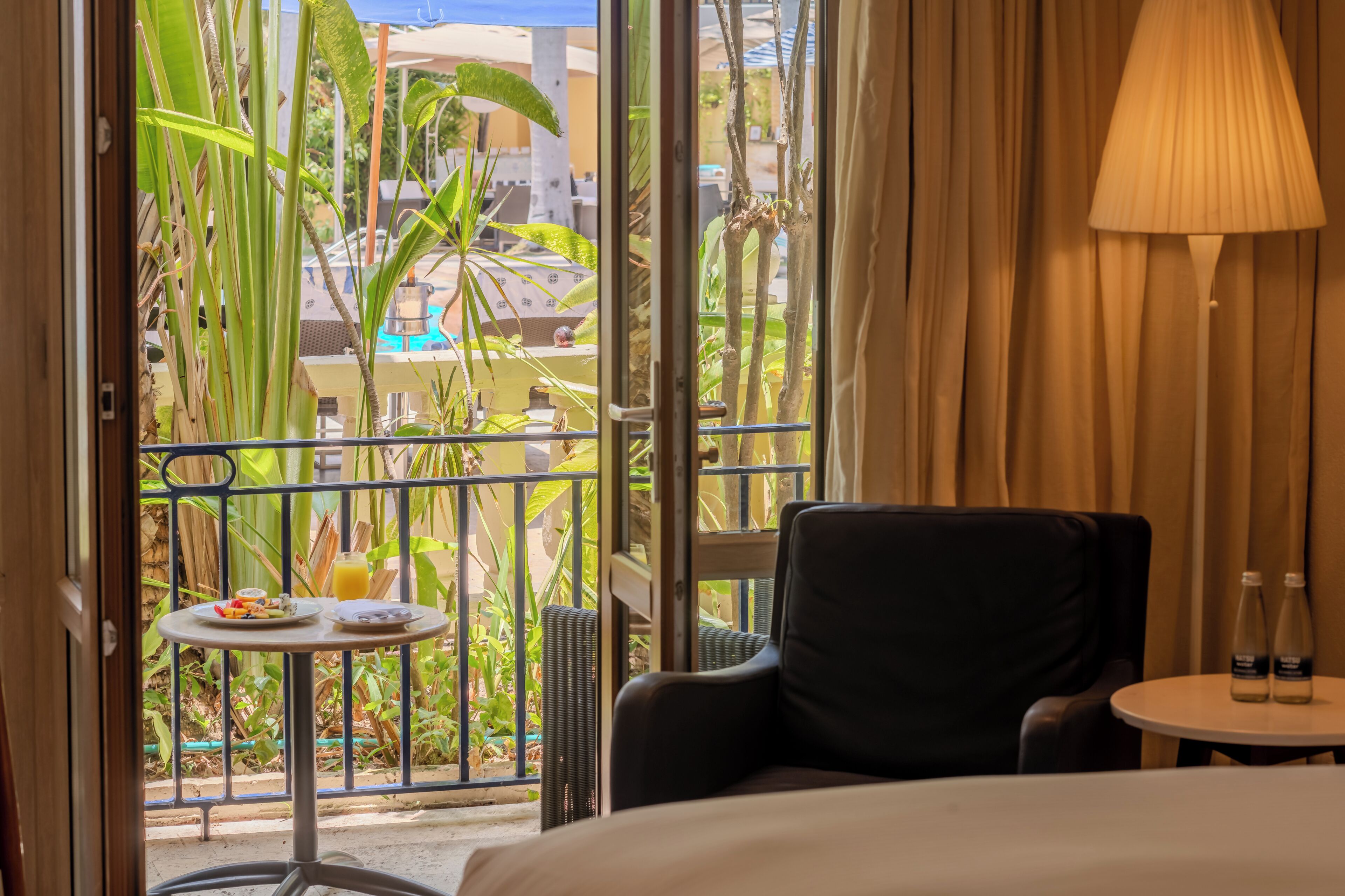 Une chambre d’hôtel avec un balcon, une table à manger avec de la nourriture et des boissons, une chaise et une lampe.