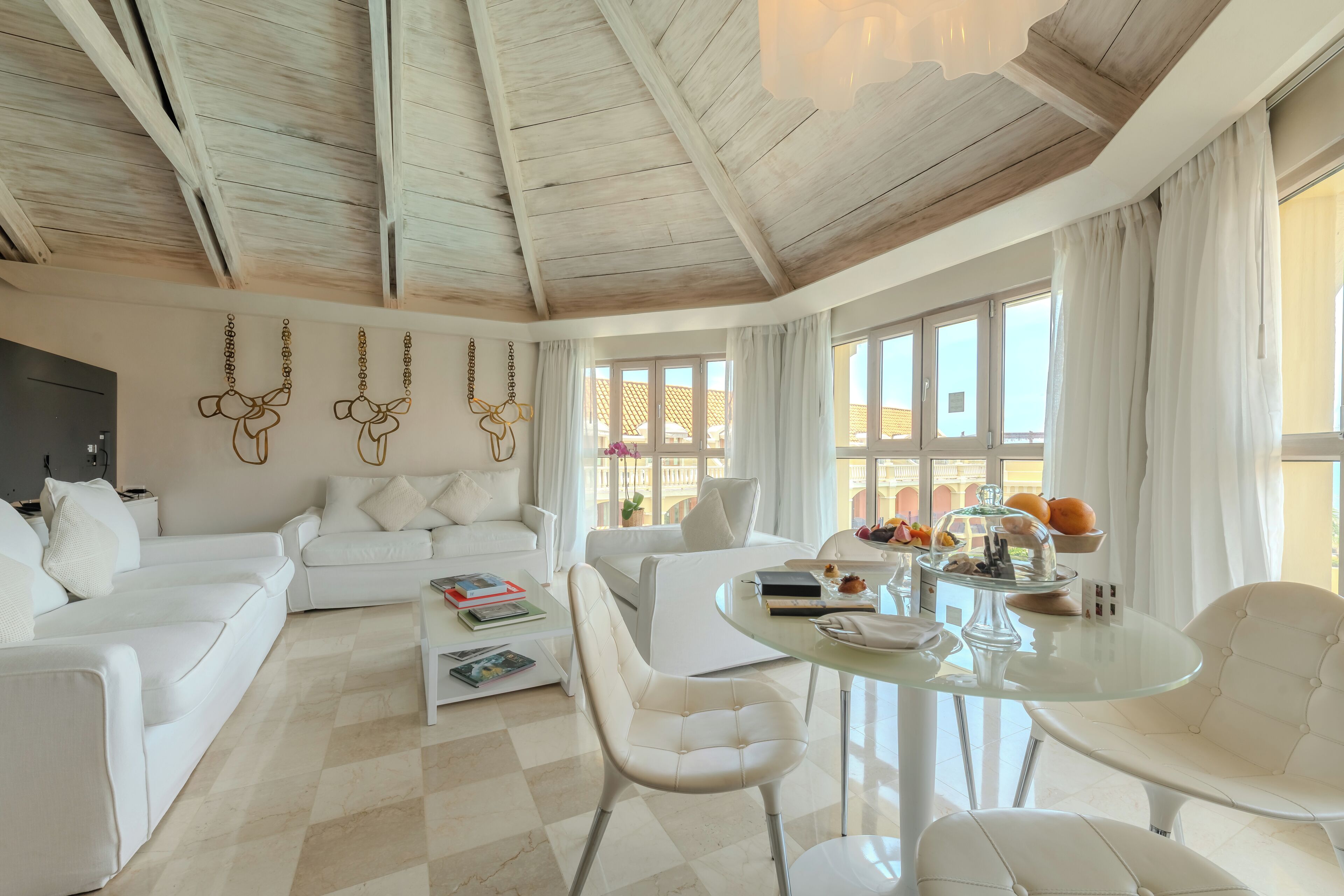 Amplia sala de estar con techo alto, muebles blancos y ventanas grandes.