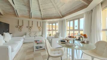 Amplia sala de estar con techo alto, muebles blancos y ventanas grandes.
