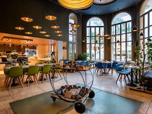 Un vaste espace dédié à la salle à manger, avec de hauts plafonds, de grandes fenêtres et un chariot rempli de plats et de produits alimentaires.