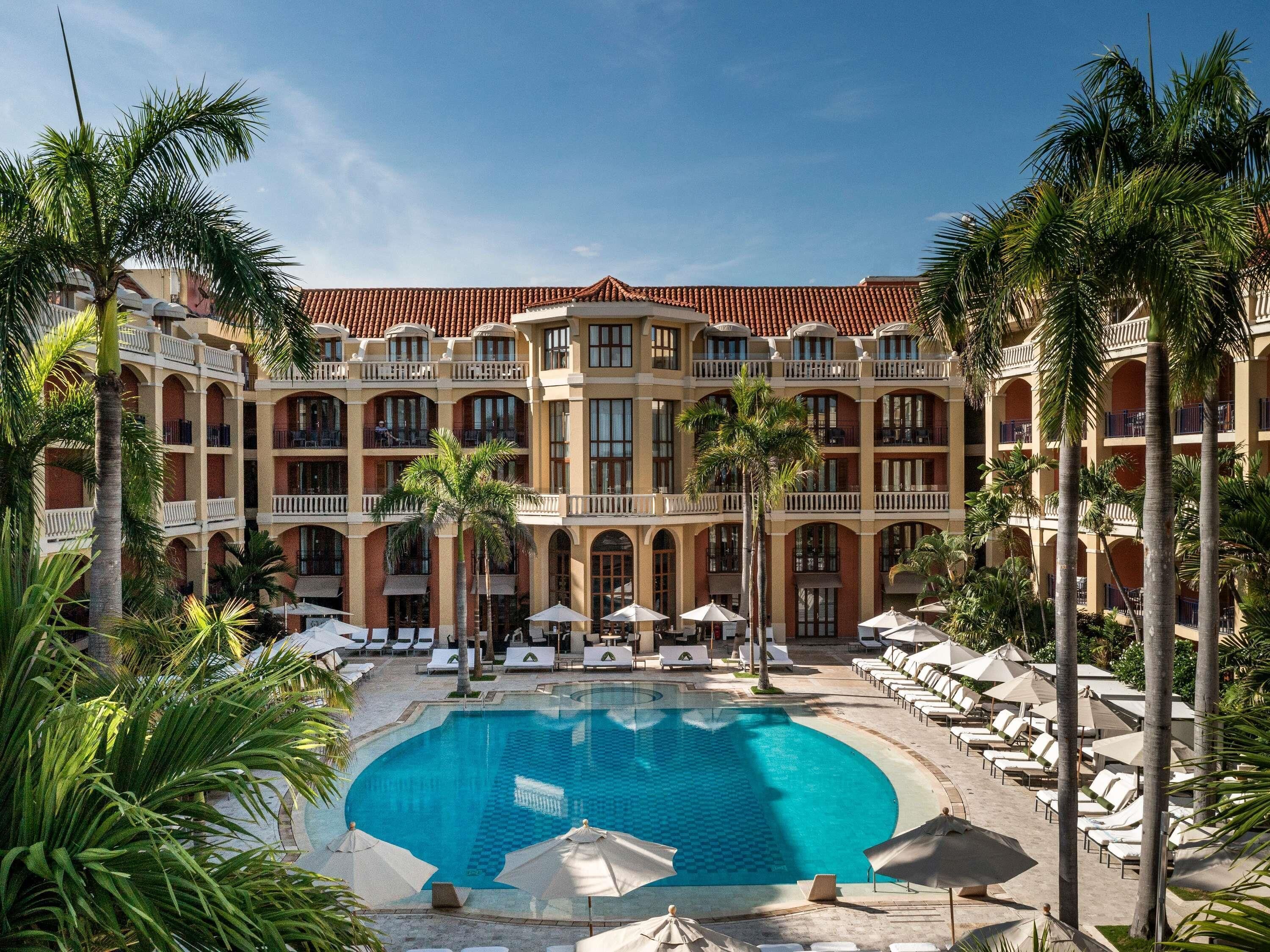Un hotel con piscina central, varios balcones y palmeras.