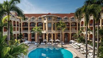 Un hotel con piscina central, varios balcones y palmeras.