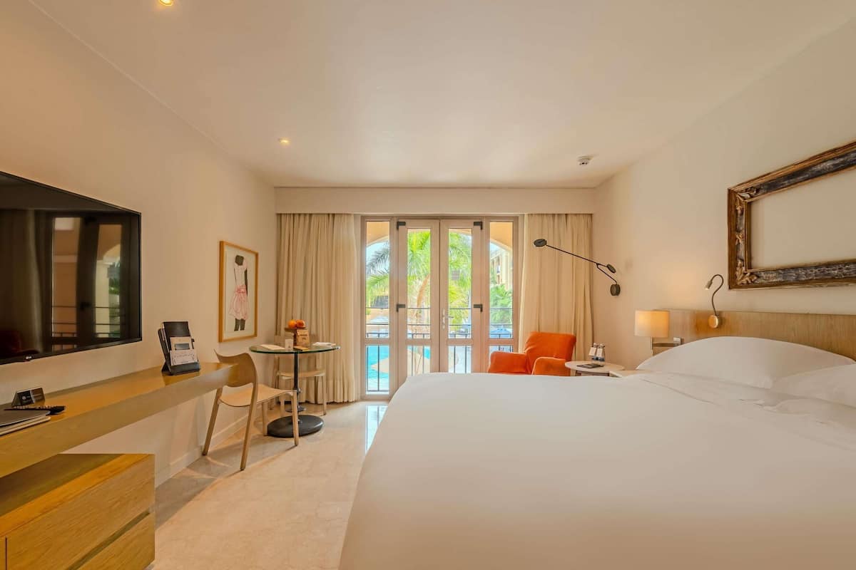 A hotel room with a bed, desk, chair, and a view of the outdoors.
