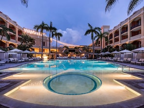 Piscina di un hotel con lettini, ombrelloni e palme.