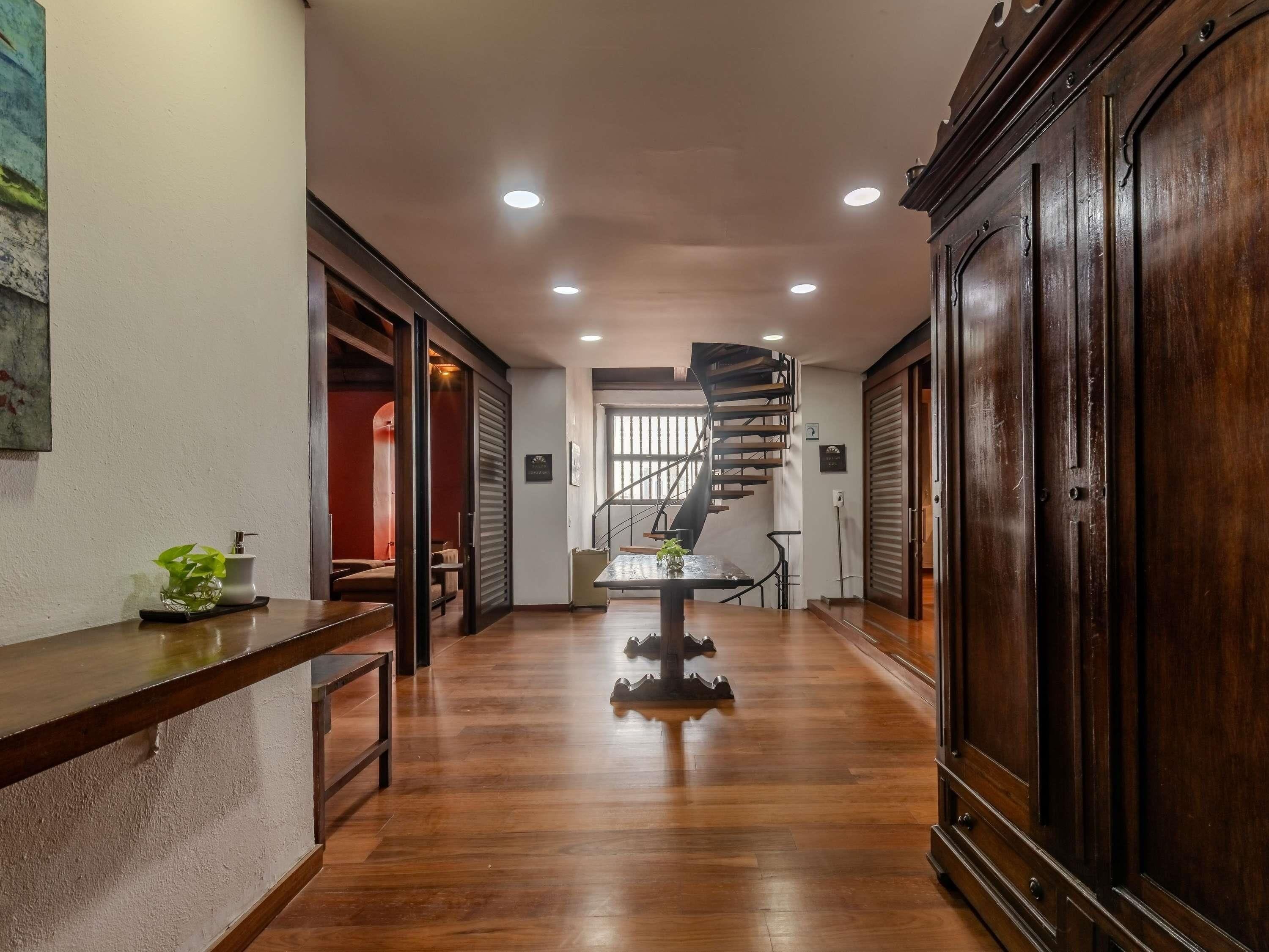 A hallway with wooden flooring, a spiral staircase, and a large wooden cabinet.