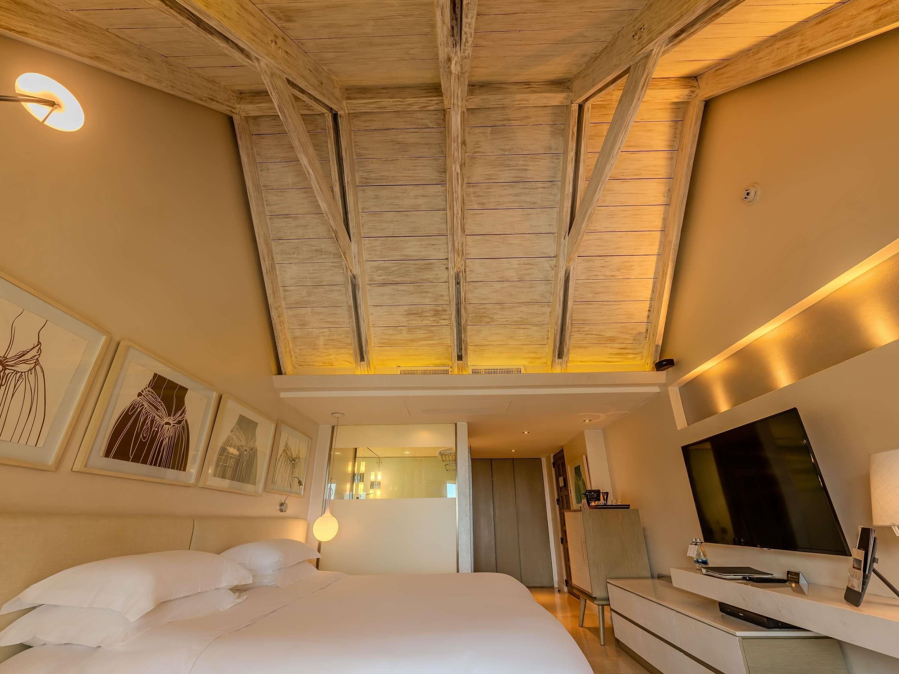 Quarto de hotel com uma cama grande, televisão de tela plana, escrivaninha com luminária e obras de arte nas paredes.
