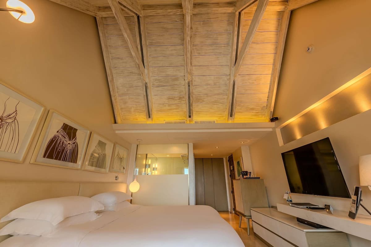Une chambre dâhĂŽtel dotĂ©e dâun grand lit, dâun tĂ©lĂ©viseur Ă Ă©cran plat, dâun bureau avec une lampe et dâĆuvres dâart accrochĂ©es aux murs.