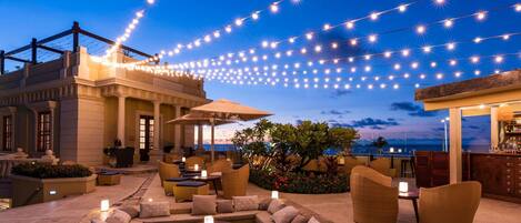 Un área de estar al aire libre con luces colgantes, piscina y bar.