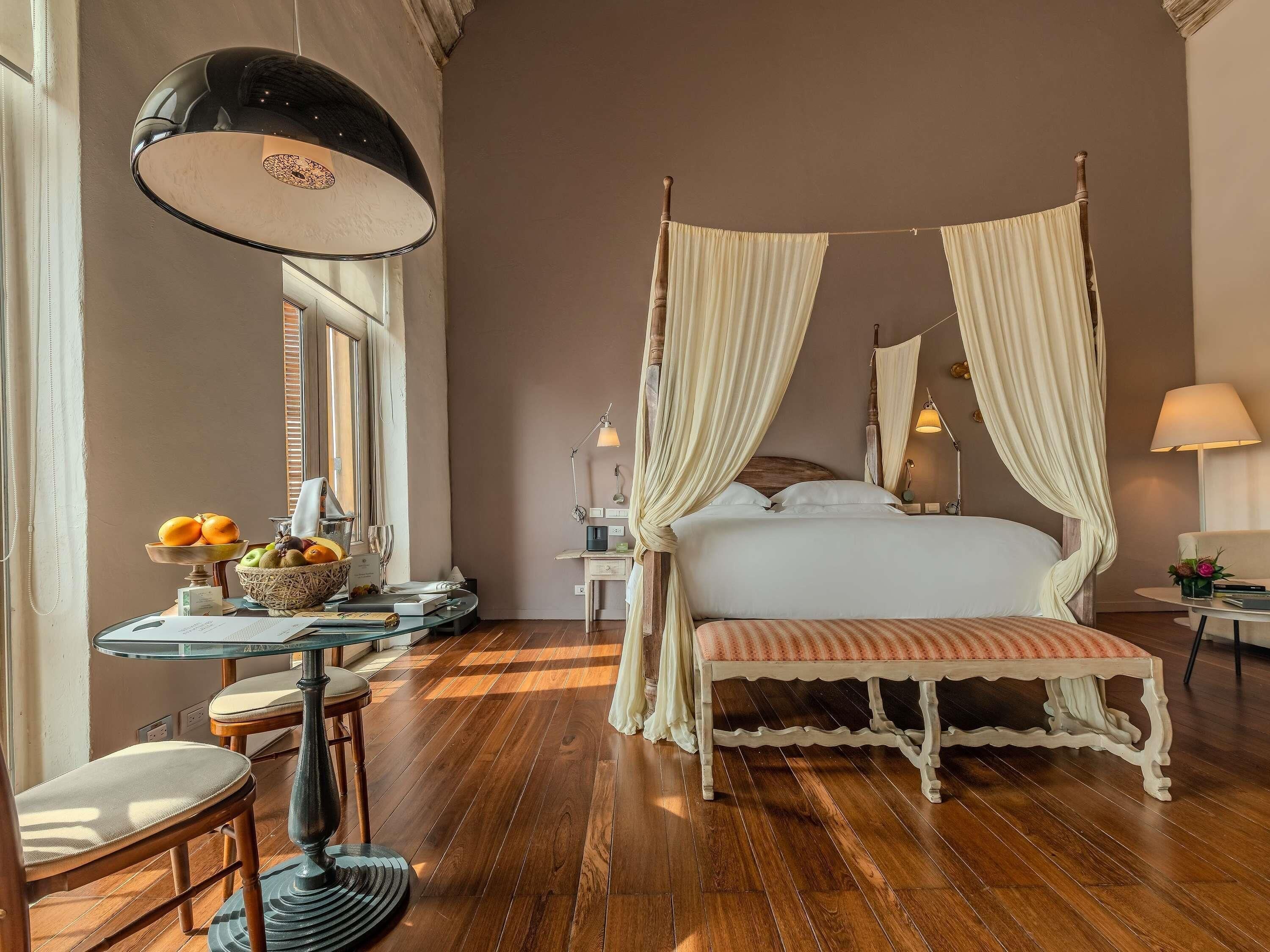 A four-poster bed with a canopy, a round table with a lamp, and a fruit bowl.