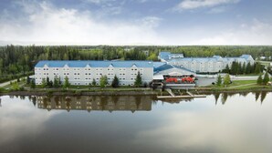 Un hôtel à plusieurs étages, doté d’un toit bleu, situé au bord d’un lac paisible et entouré d’une forêt dense.