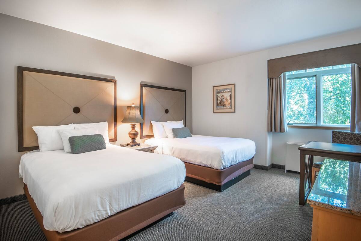 A hotel room with two beds, a desk, and a window with curtains.
