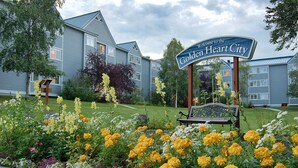 Un panneau d’accueil indiquant l’entrée de Golden Heart City, entouré d’un jardin où poussent différentes sortes de fleurs.