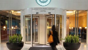 Sheraton Paris Airport -hotellin sisäänkäynti, jossa on lasiovi, ruukuissa olevia kasveja ja ovelle kiinnitetty kyltti.
