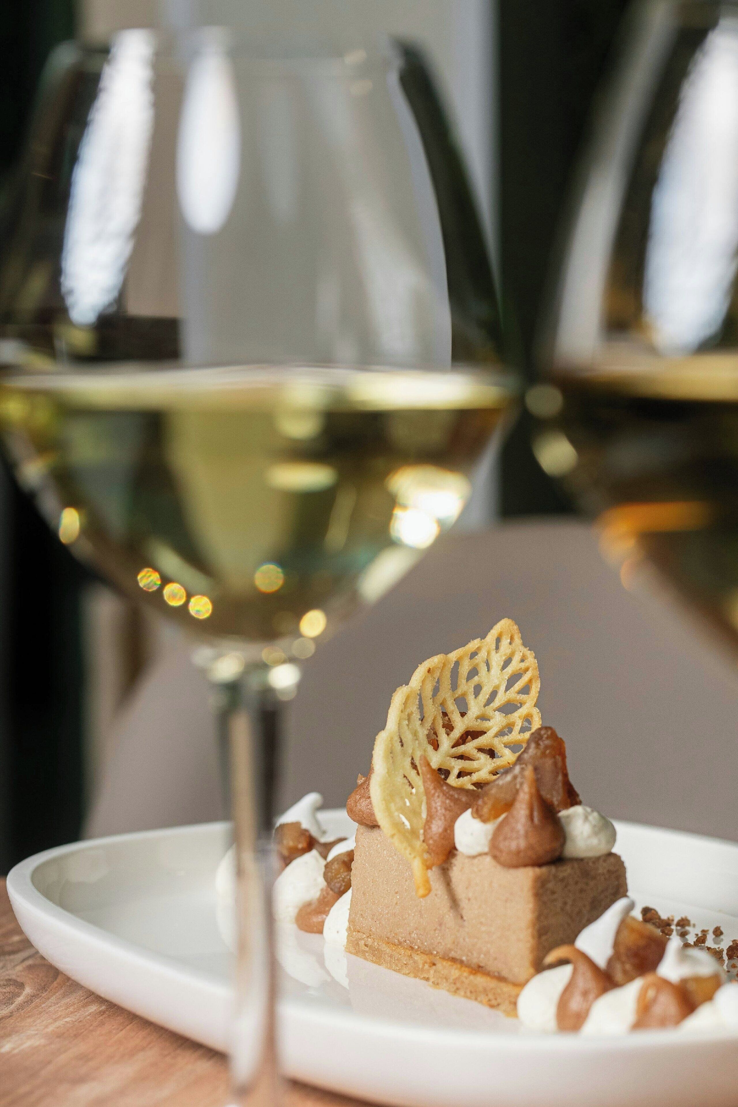 A dessert with a leaf garnish on a plate, accompanied by a glass of white wine.
