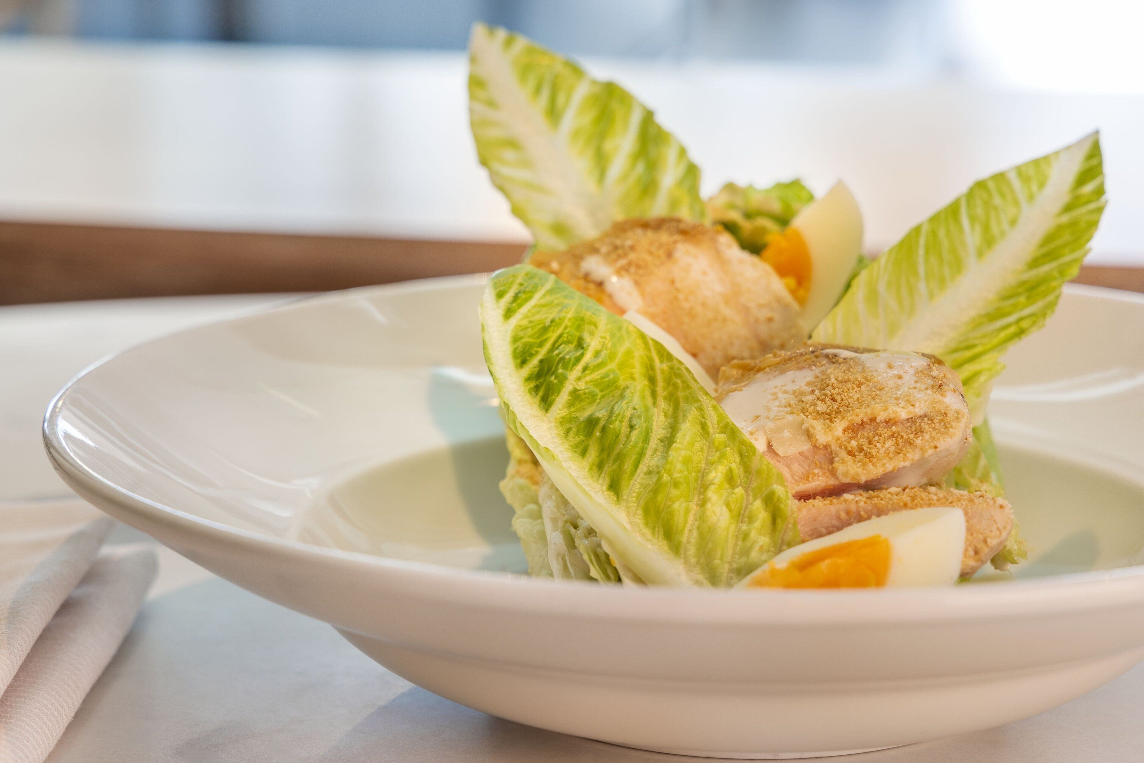 Un plato blanco con una ensalada de lechuga, un trozo de pollo empanizado y una rodaja de naranja.