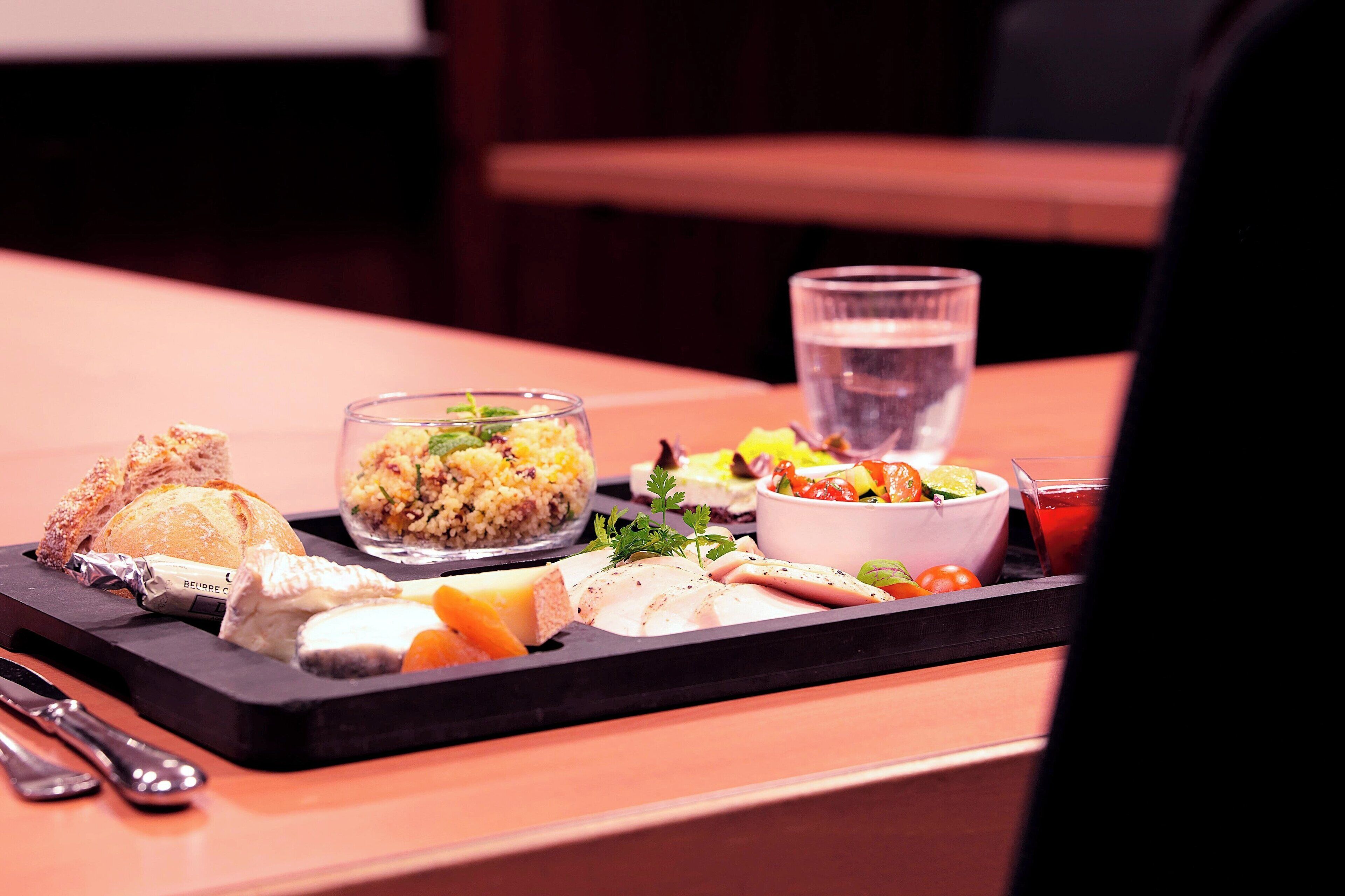 A tray with various food items including bread, cheese, and a salad, along with a glass of water.