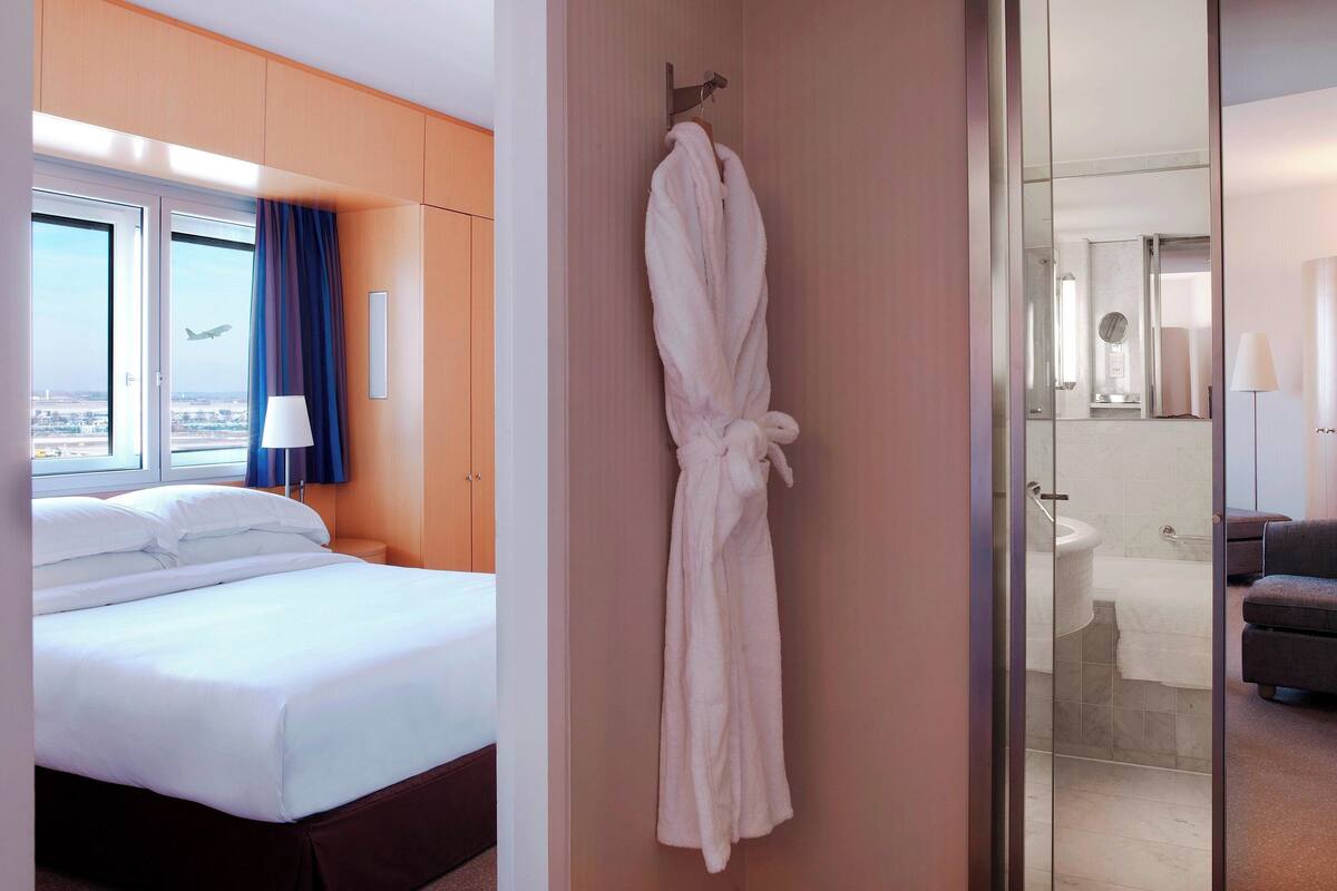 Habitación de hotel con cama, bata colgada en la pared y vista a la ciudad desde la ventana.