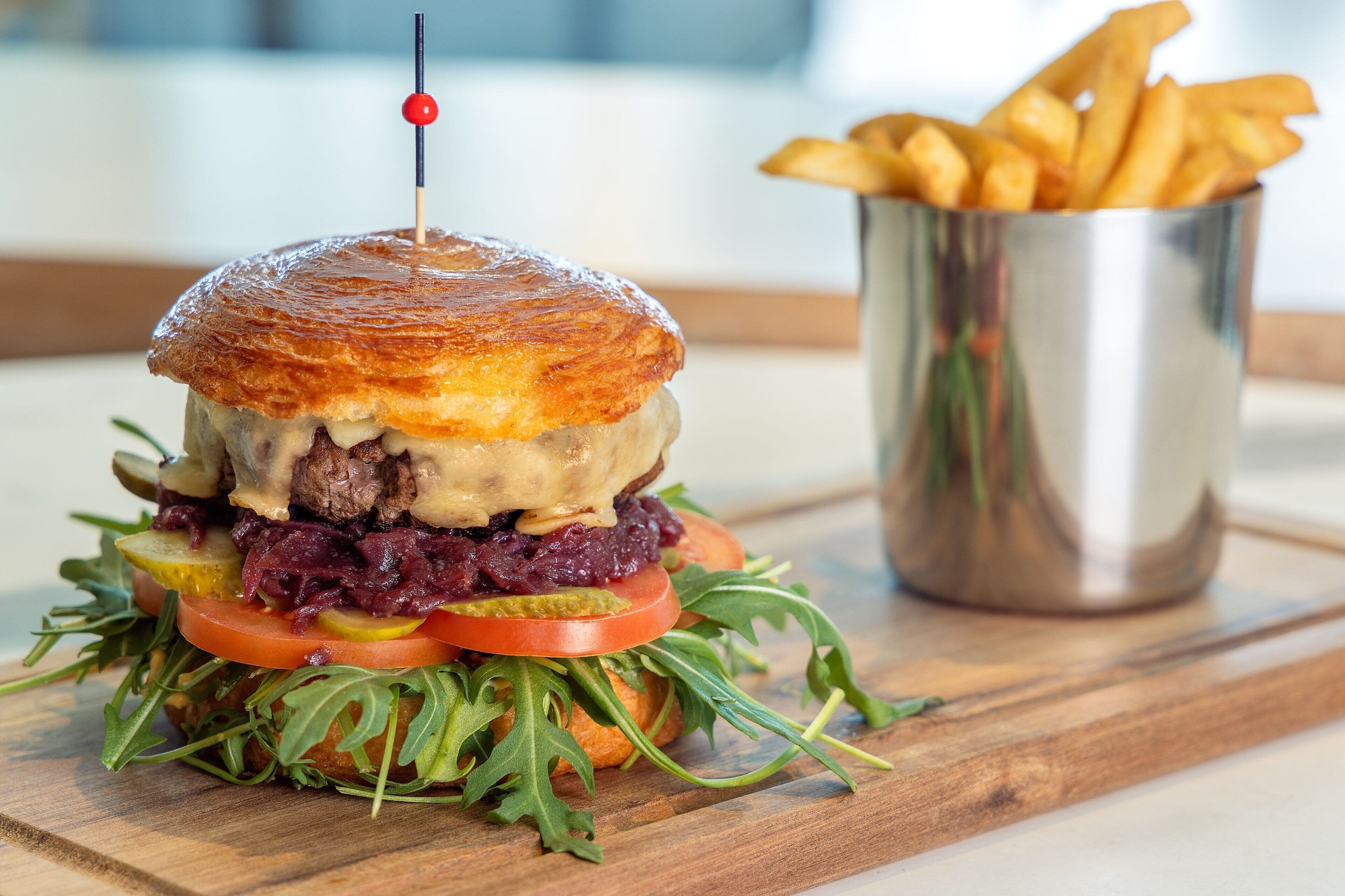 Een gourmetburger met geroosterd broodje, gegarneerd met een rode spies, vergezeld van friet.