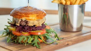 Een gourmetburger met geroosterd broodje, gegarneerd met een rode spies, vergezeld van friet.