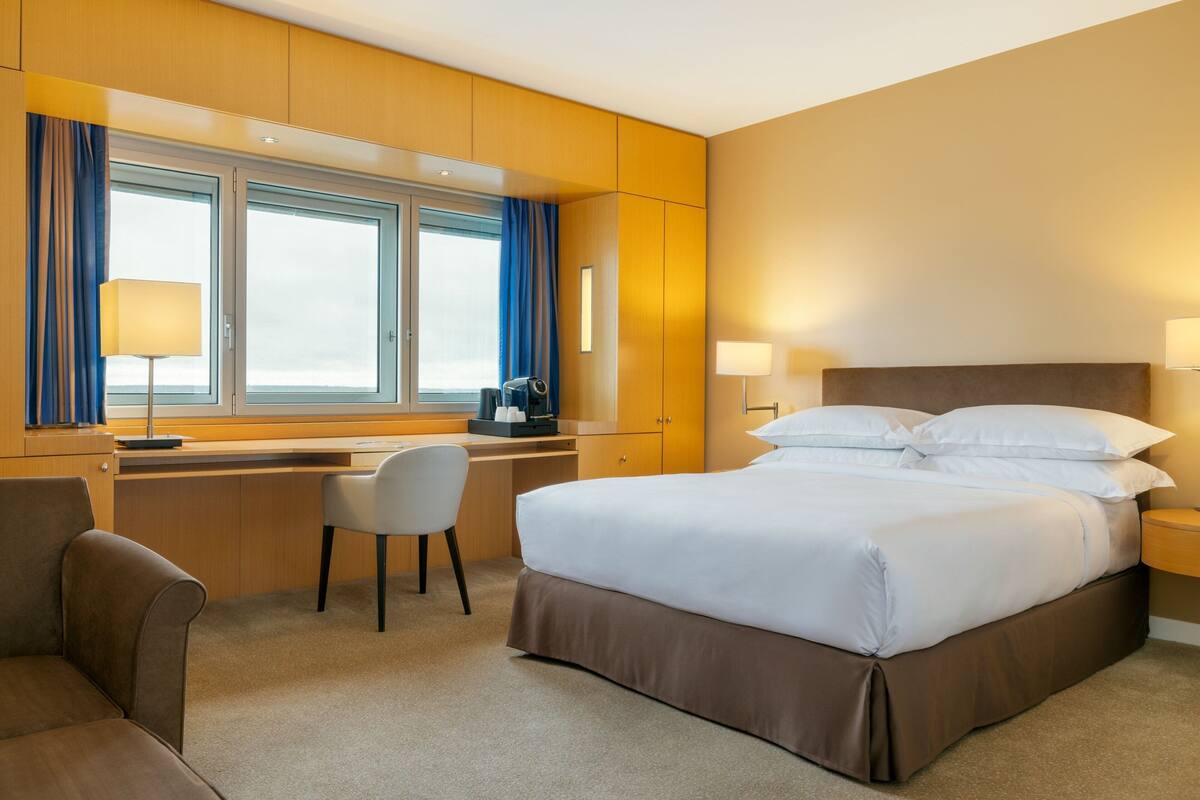 Habitación de hotel con cama, escritorio, silla y ventana con cortinas.