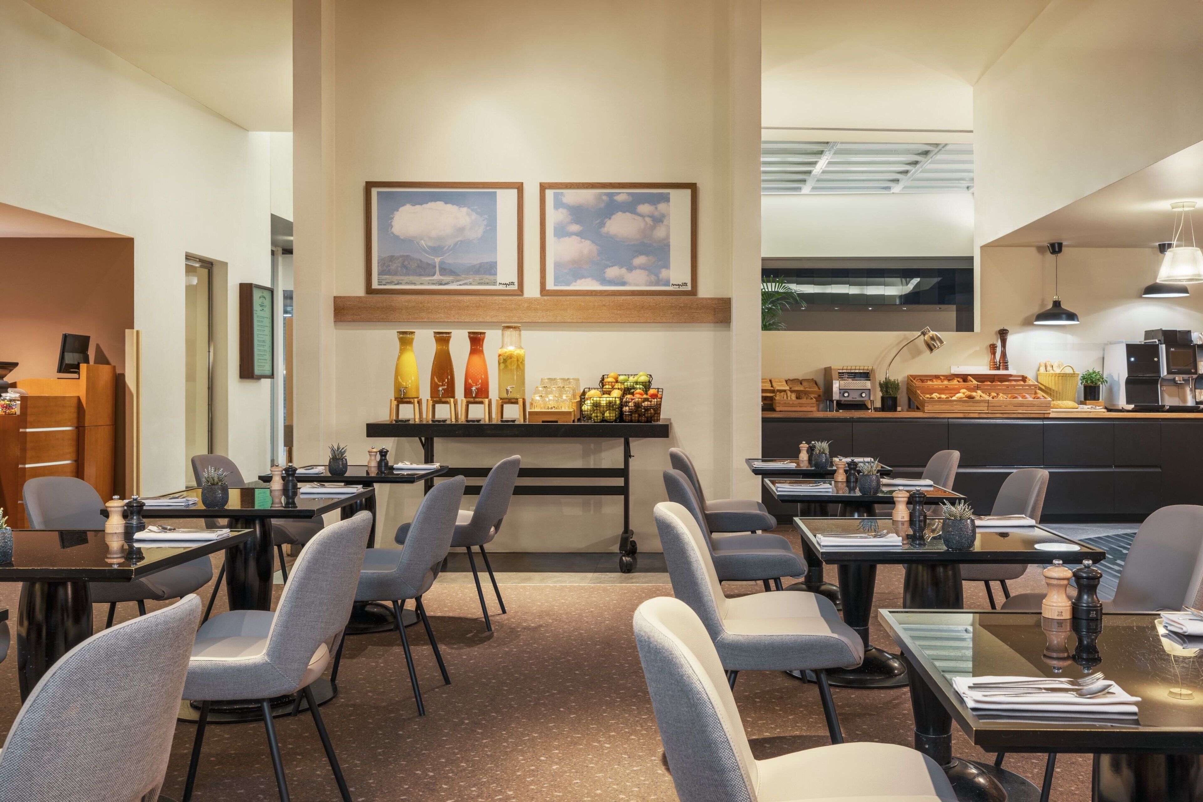 A modern restaurant with tables and chairs, a counter with food items, and framed pictures on the wall.