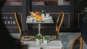 An outdoor dining area with a table set for two, surrounded by wicker chairs. A glass wall displays a wine rack and the text "SAISONS." - Sheraton Paris Charles de Gaulle Airport Hotel (Tremblay-en-France)