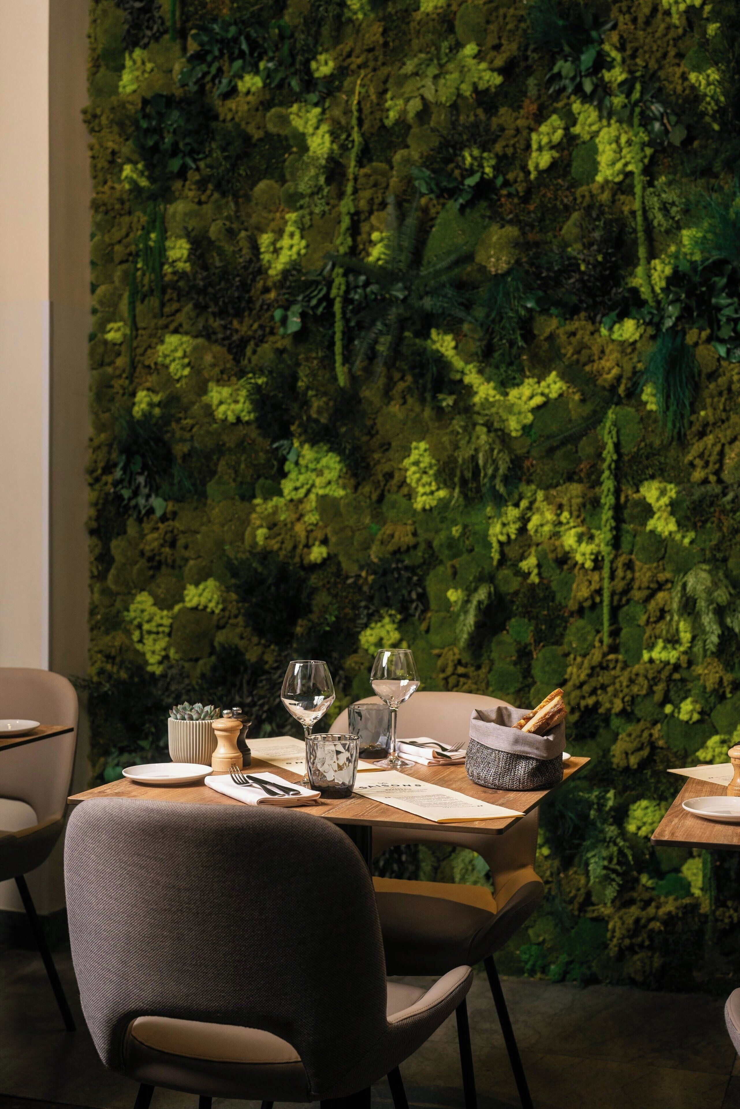 A dining area with a table set for two, a moss wall, and a wooden table.