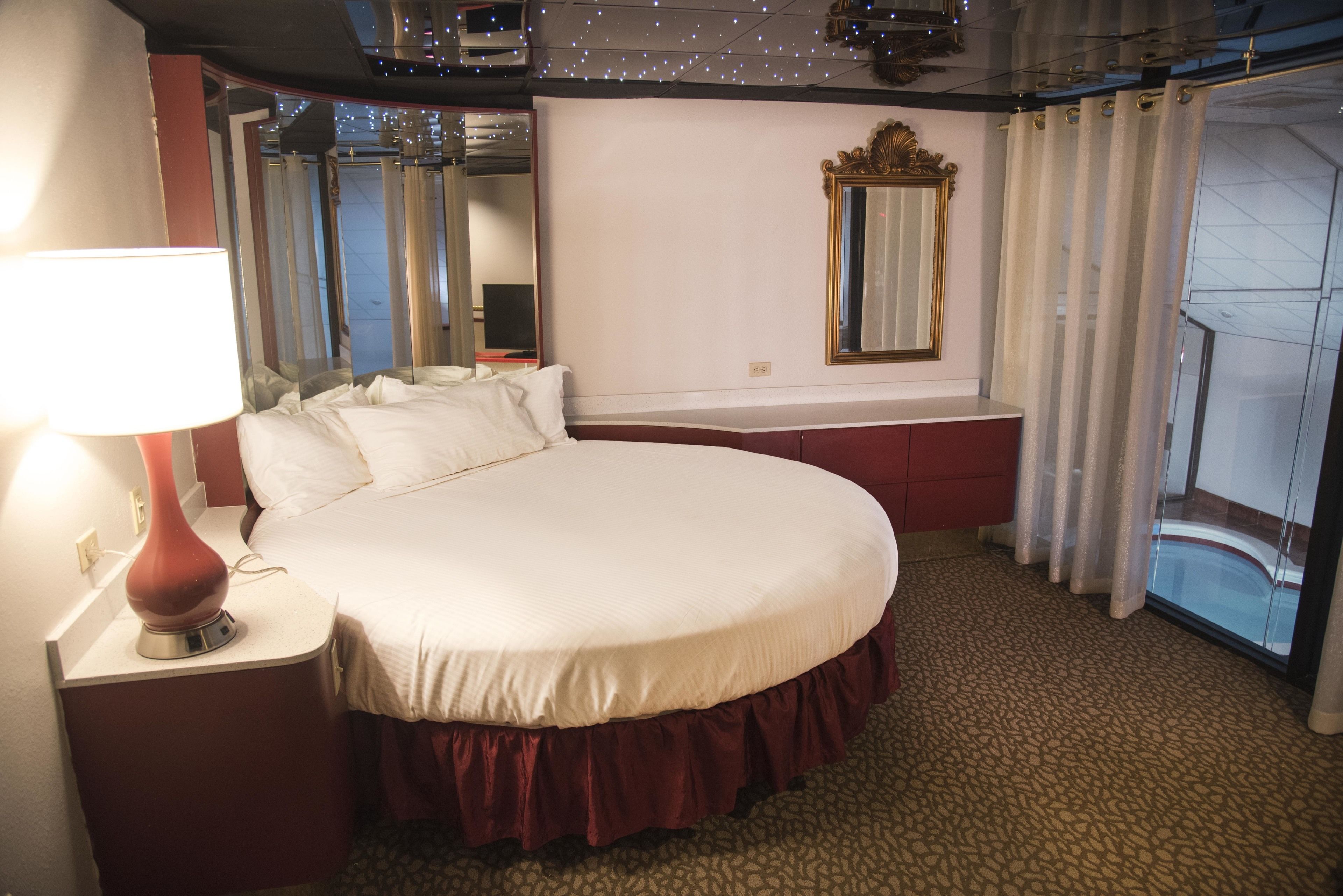A hotel room with a large bed, a bedside lamp, a mirror, and a view of the outside.