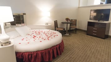 A hotel room with a large bed, a desk, a chair, a TV, and a mirror.