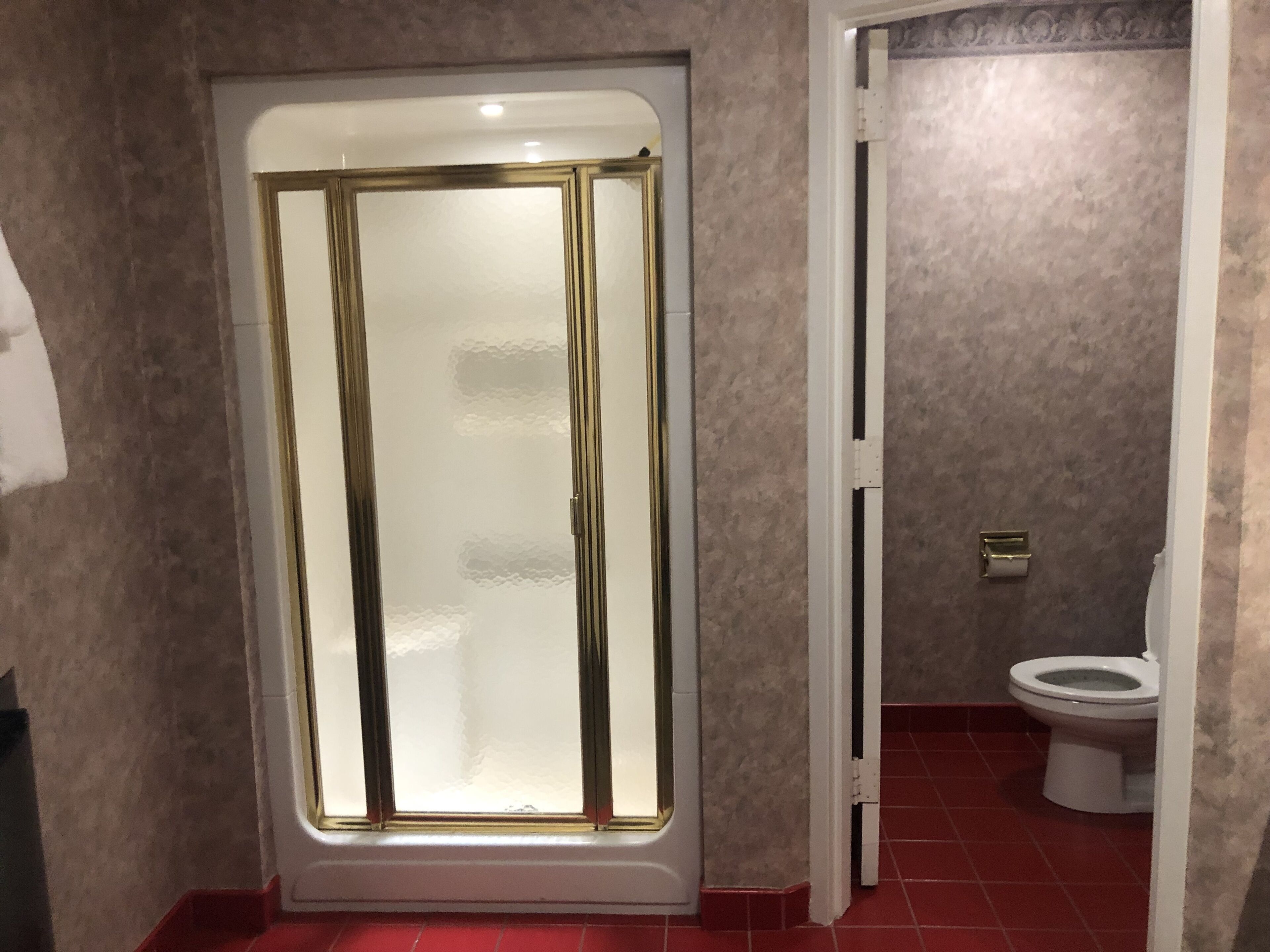 A bathroom with a glass-enclosed shower, a toilet, and a red-tiled floor.