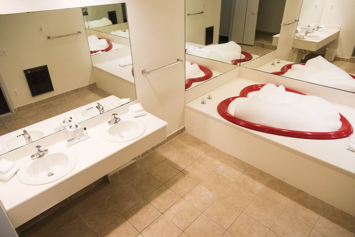 Une salle de bain moderne avec trois lavabos, un grand miroir et une baignoire rouge.