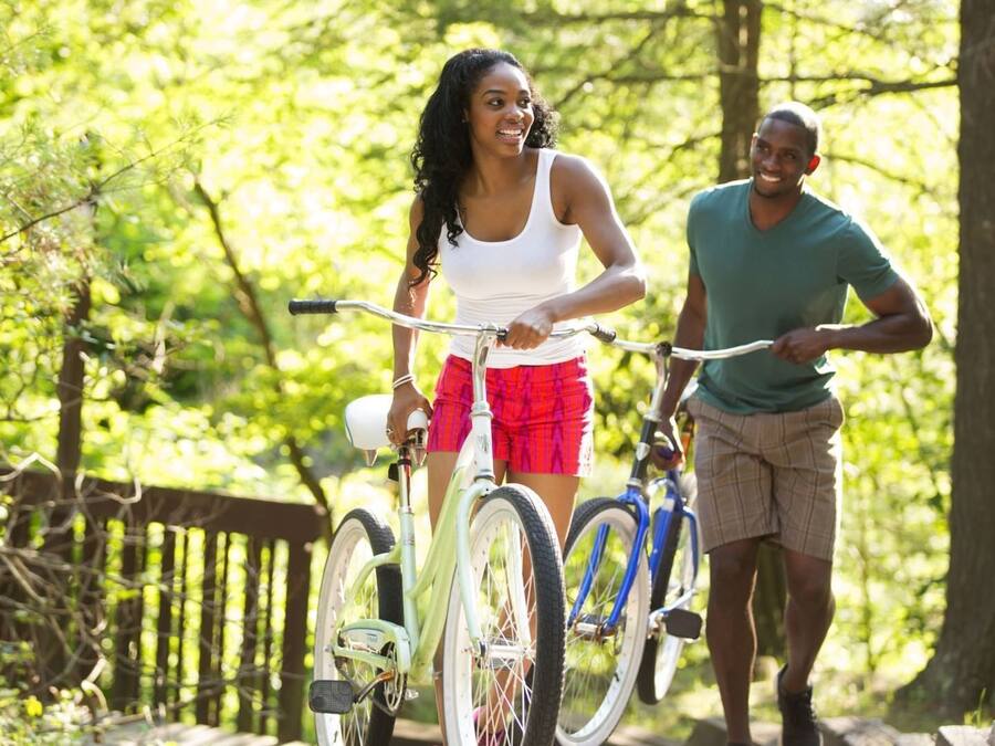 Two people walking and riding bicycles in a wooded area.