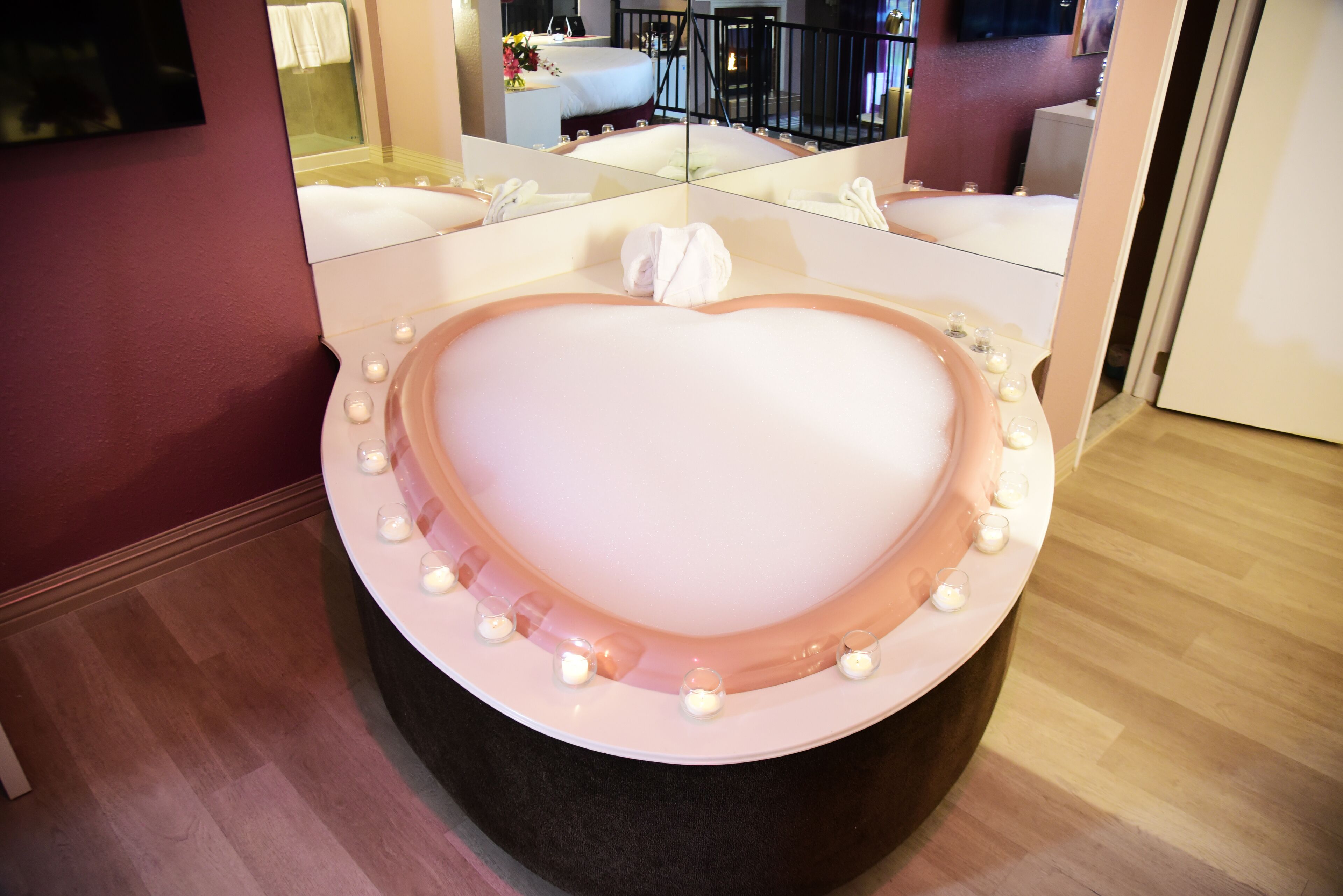 A heart-shaped bathtub with candles and a towel, surrounded by mirrors.