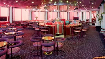 Amplia zona de bar con diversas opciones de asientos, incluyendo mesas redondas y taburetes de bar.