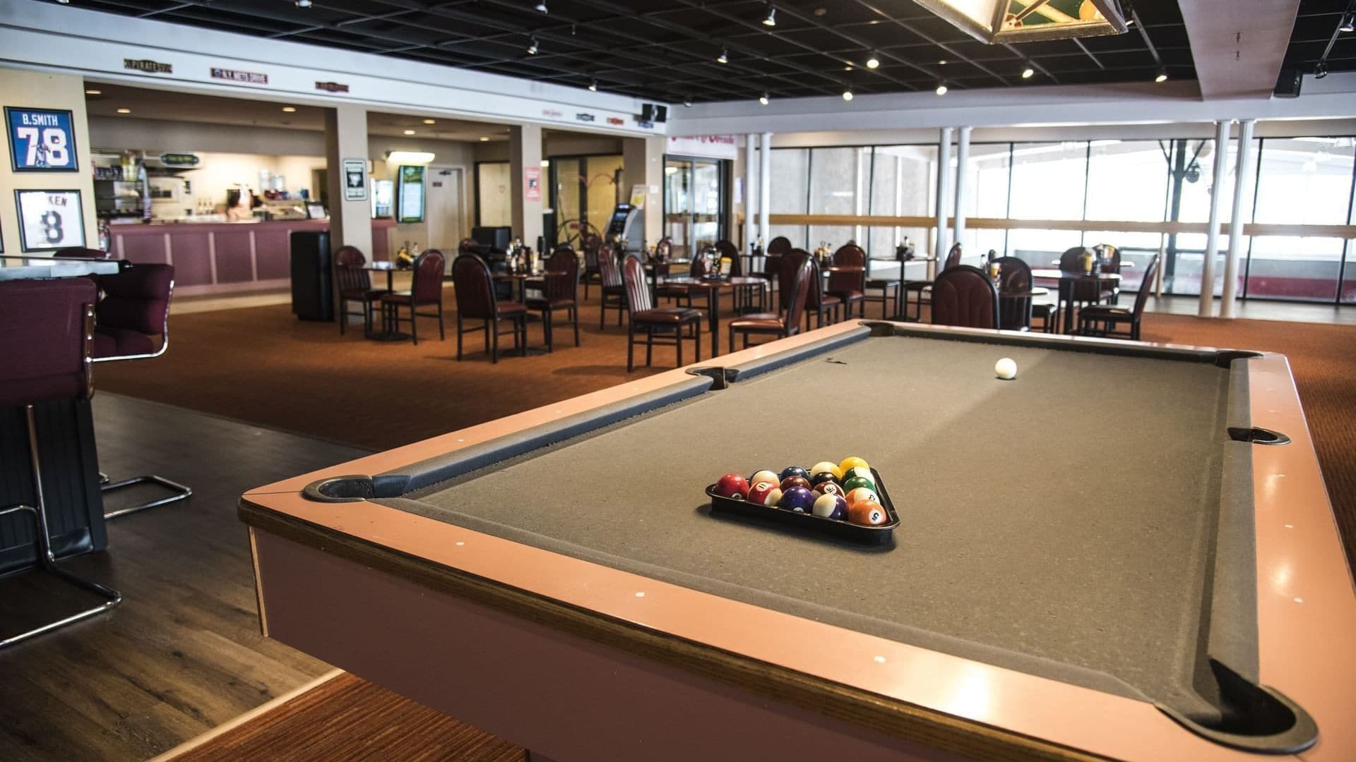 A pool table with balls in a room with multiple tables and chairs, a bar area, and large windows.