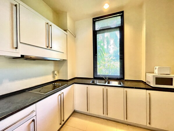 A kitchen with white cabinets, a black countertop, a stainless steel sink, and a microwave. - The Westin Langkawi Resort & Spa (Langkawi)