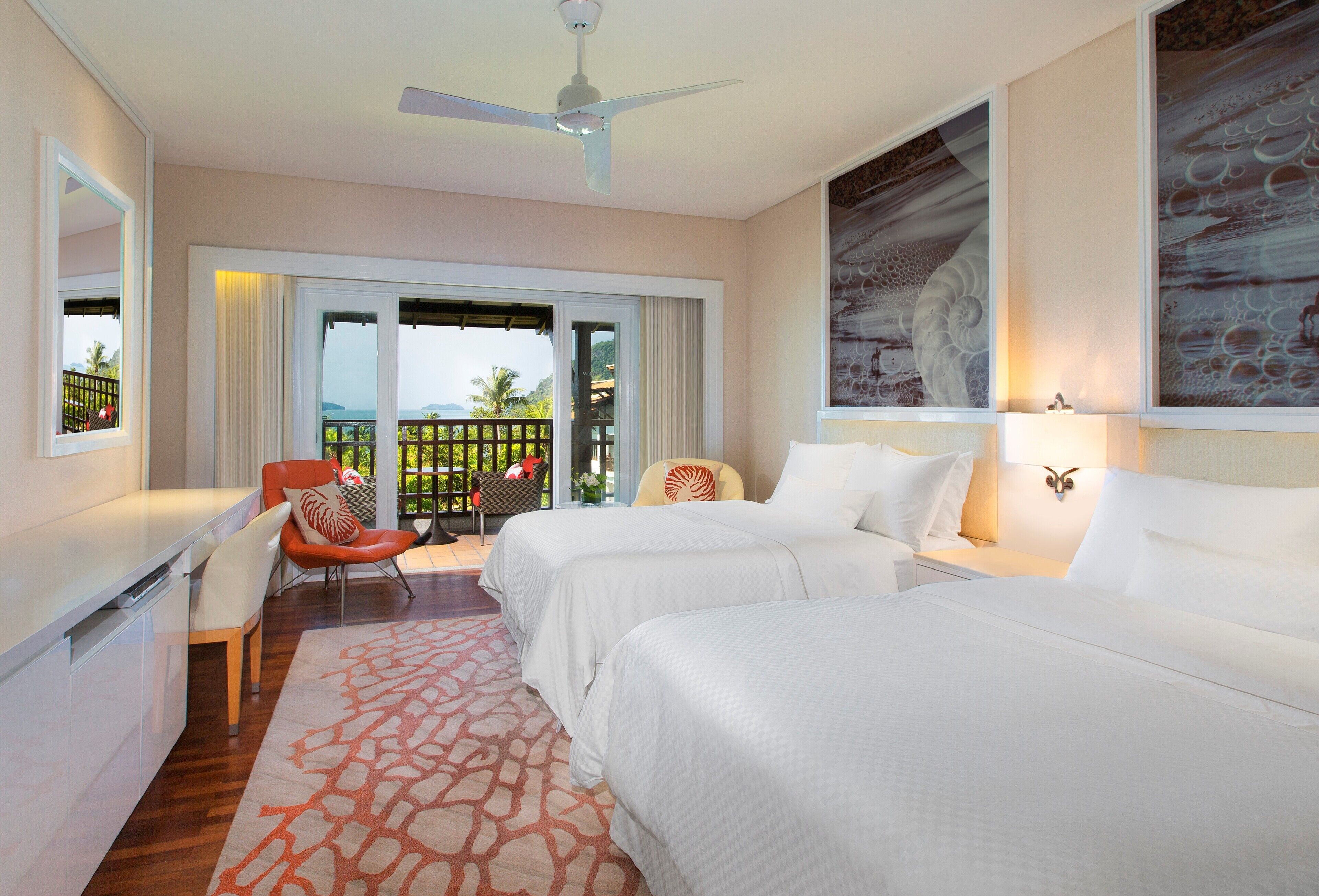 A hotel room with two beds, a desk, a chair, and a balcony with a view.