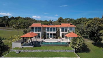 Een modern huis met twee verdiepingen, een zwembad, een overdekt terras en een verzorgd gazon.