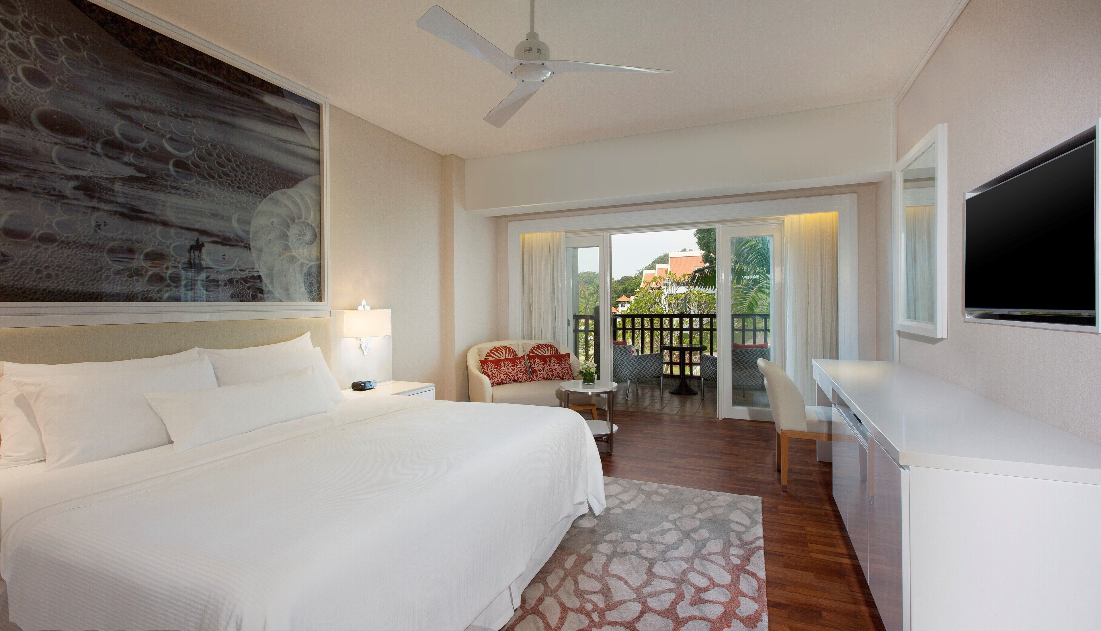 A hotel room with a large bed, a desk, a chair, a TV, and a balcony with a view of the city.